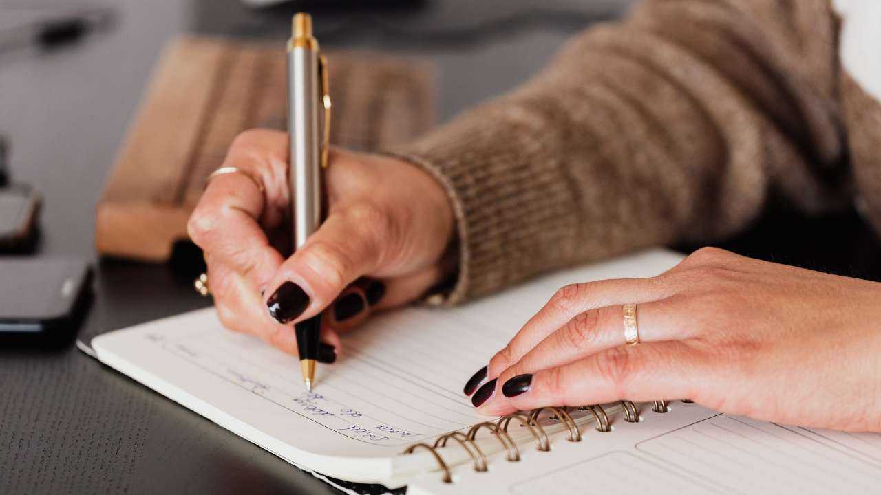 Крупным планом тетрадь, в которой женщина записывает ручкой свои базовые финансовые навыки, чтобы их подтянуть
