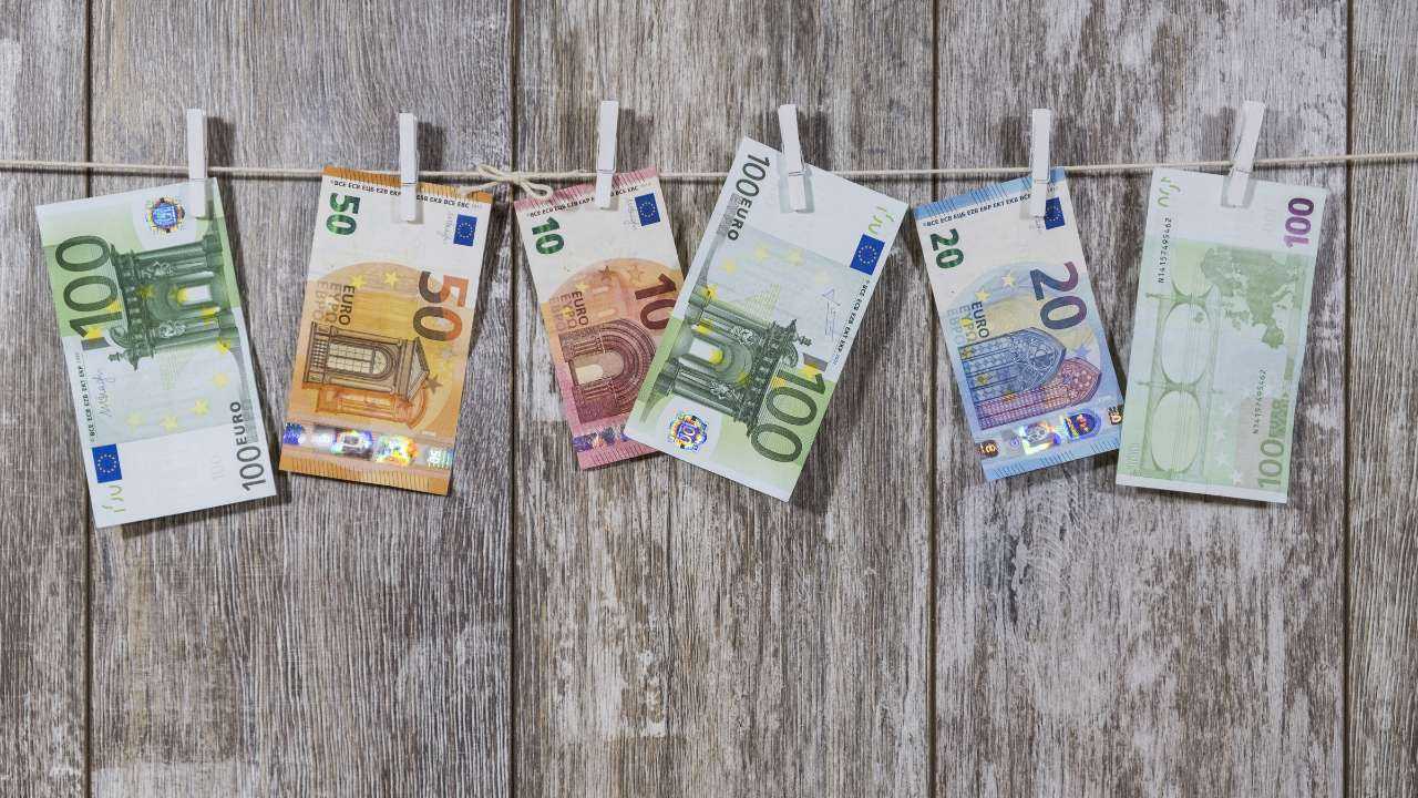 Перед деревяным фоном на веревке за прищепки развешены купюры евро – фиатные деньги Евросоюза и Латвии