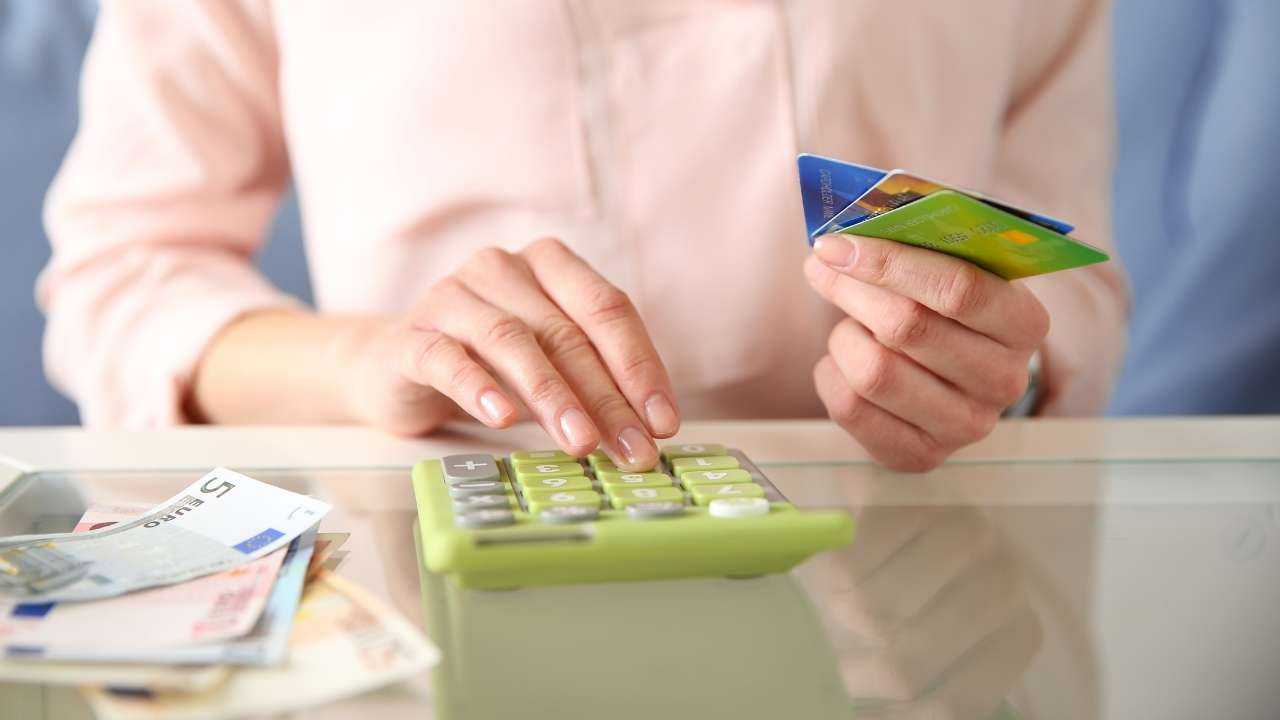 Sieviete skaita uz kalkulatora, turot rokā kredītkarti, savus neparedzētos izdevumus