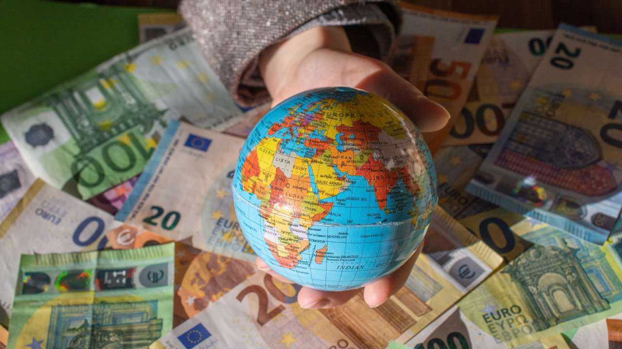 Cilvēka roka tur globusu uz eiro banknošu fona, simbolizējot iespējas kredītam ārzemēs strādājošiem