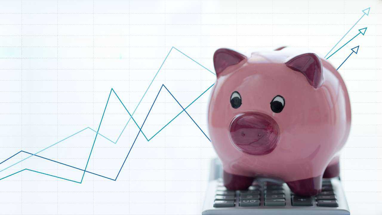 Cūciņa-krājkasīte stāv uz kalkulatora un fonā grafiki, kas atspoguļo inflācijas ietekmi uz procentu likmēm