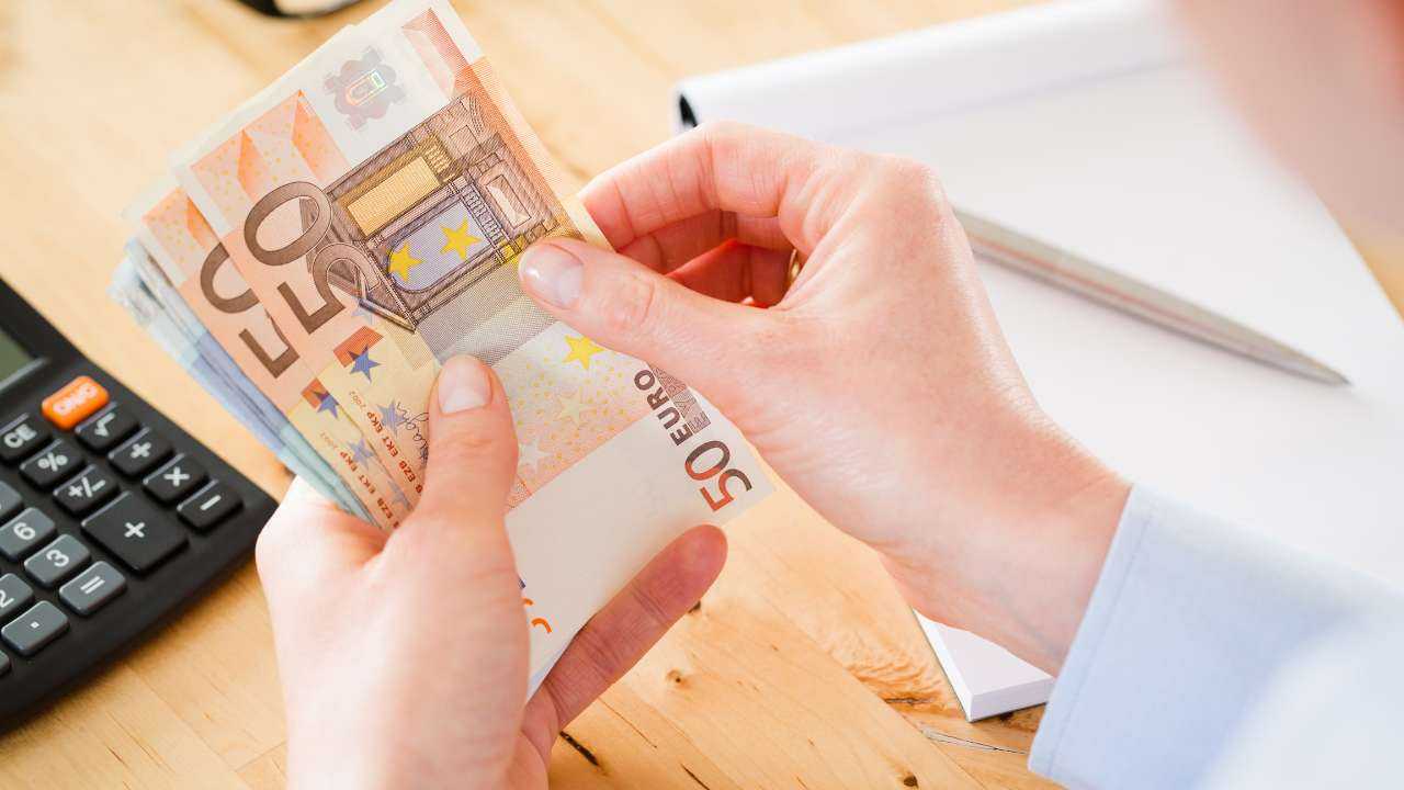 На фоне письменного стола с калькулятором и записями женские руки пересчитывают евро банкноты полученного денежного займа