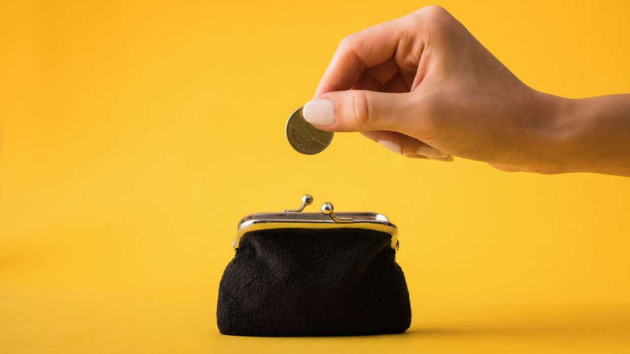Uz dzeltena fona sievietes roka liek 50 centus mazā melnā maciņā, jo uzzināja, kā ietaupīt naudu, aizņemoties