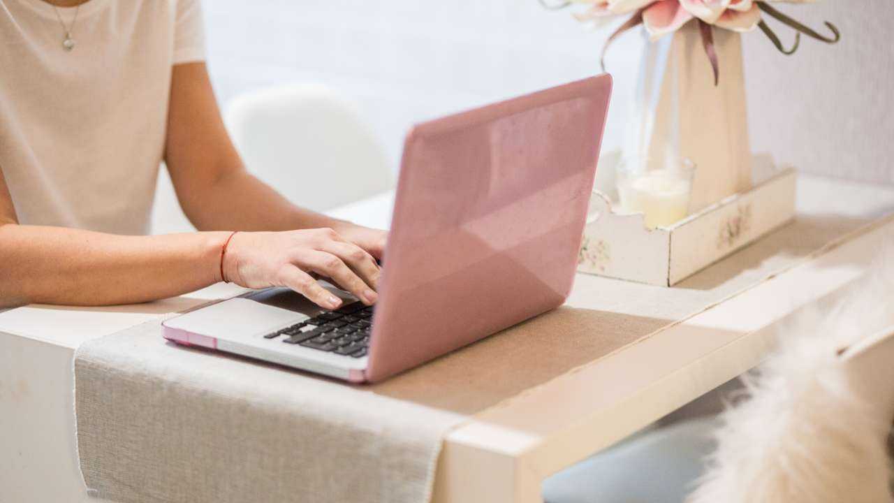 Девушка без лица сидит за столом, на котором стоит ваза, и через ноутбук в интернете, где оформить кредиты для иностранцев
