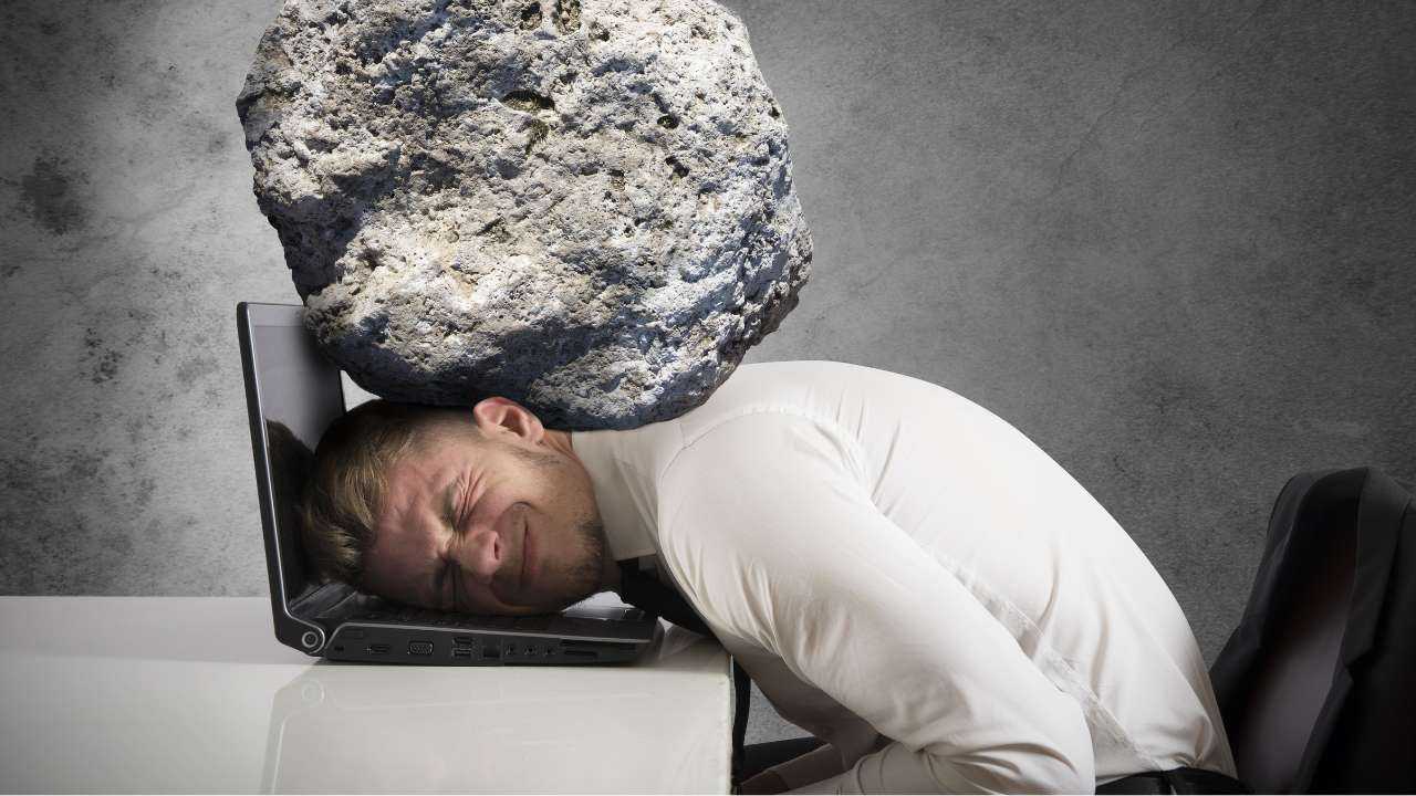 Vīrieša galvu pie datora piespiedis liels smags akmens, līdzīgi, kā spiež finansiālais stress ikdienā
