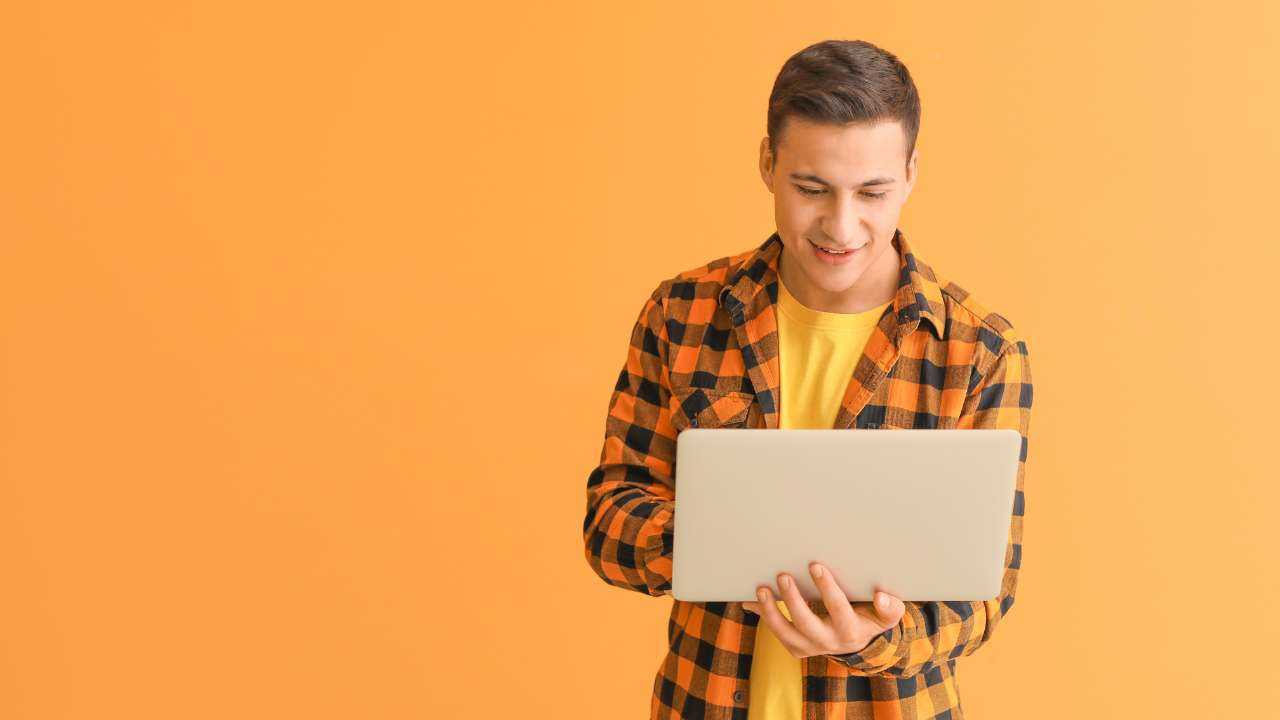 Uz dzeltena fona stāv smaidīgs vīrietis, kas no planšetes internetā meklē, kur ir iespējams iegūt aizdevumu ātri un vienkārši