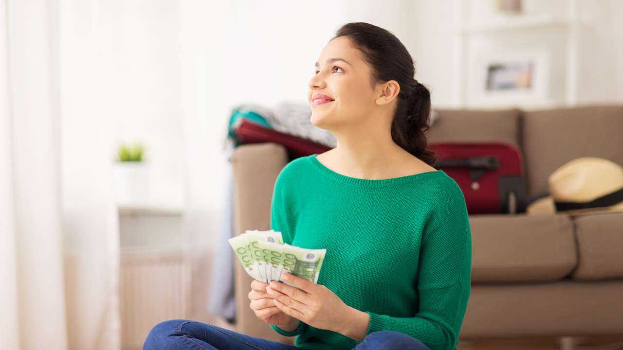 Sieviete zaļā džemperī sēž uz grīdas ar 600 eiro rokās un plāno dzimšanas dienas svinības, jo saņēma lielo notikumu kredītu