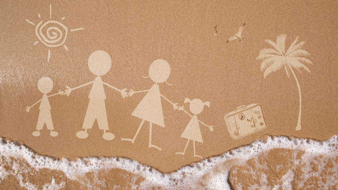 Uz smiltīm pie jūras uzzīmēta ģimene ar 2 bērniem, saule, čemodāns un palma – vasaras aktivitātes var sākties
