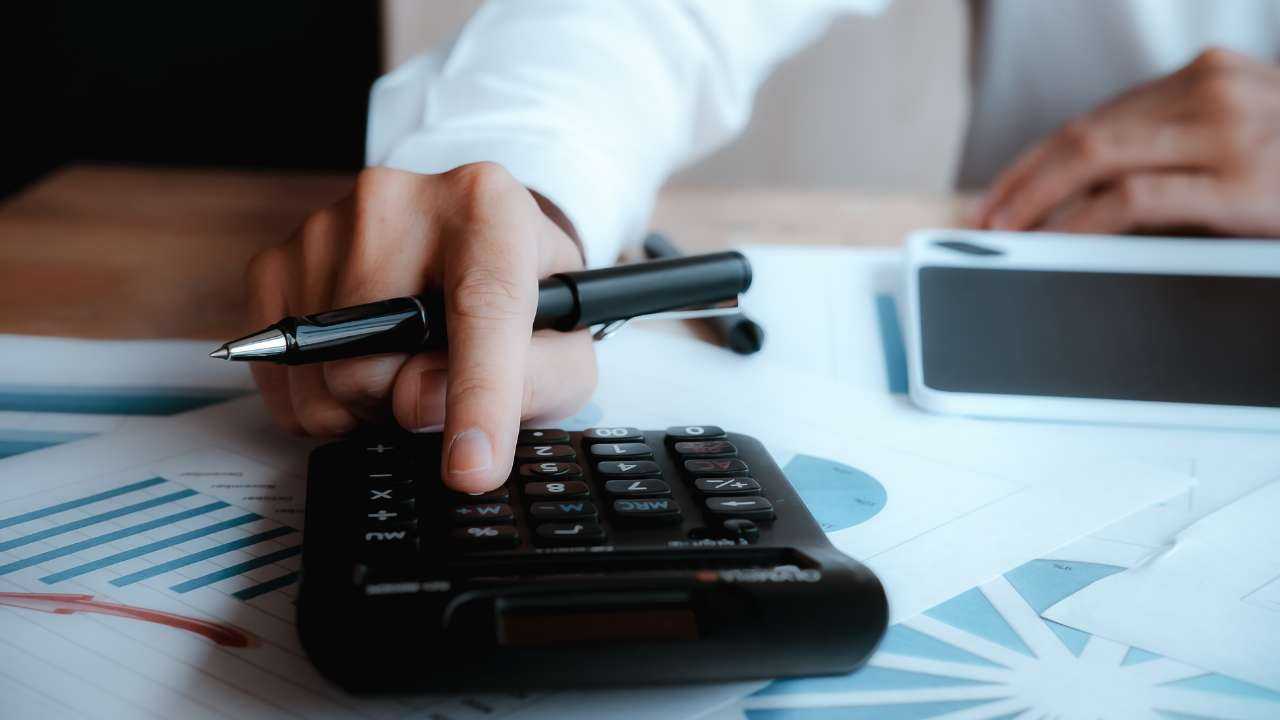 Человек держит ручку и считает на калькуляторе месячные расходы, чтобы научится правильному управлению кредитами