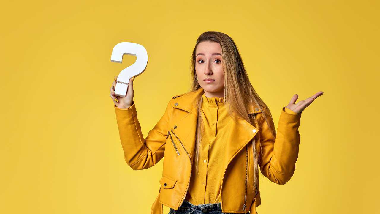Девушка в желтой куртке держит в руке знак вопроса, потому что задается вопросом, существует ли кредит для всех