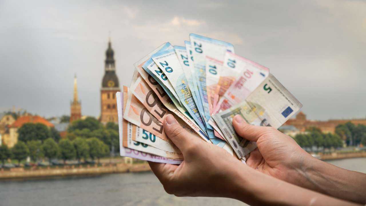 Заемщик на фоне Риги в руках держит веер из евро купюр – кредиты в Латвии доступны для заимствования