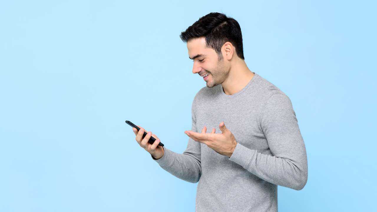 Мужчина с улыбкой смотрит на свой смартфон, находя информацию о рефинансировании кредитов без залога и поручителей