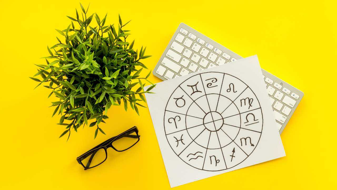 Uz dzeltena fona zaļš augs, datora klaviatūra, brilles un astroloģisks apli, jo ir gatavs naudas horoskops 2023. gada martam