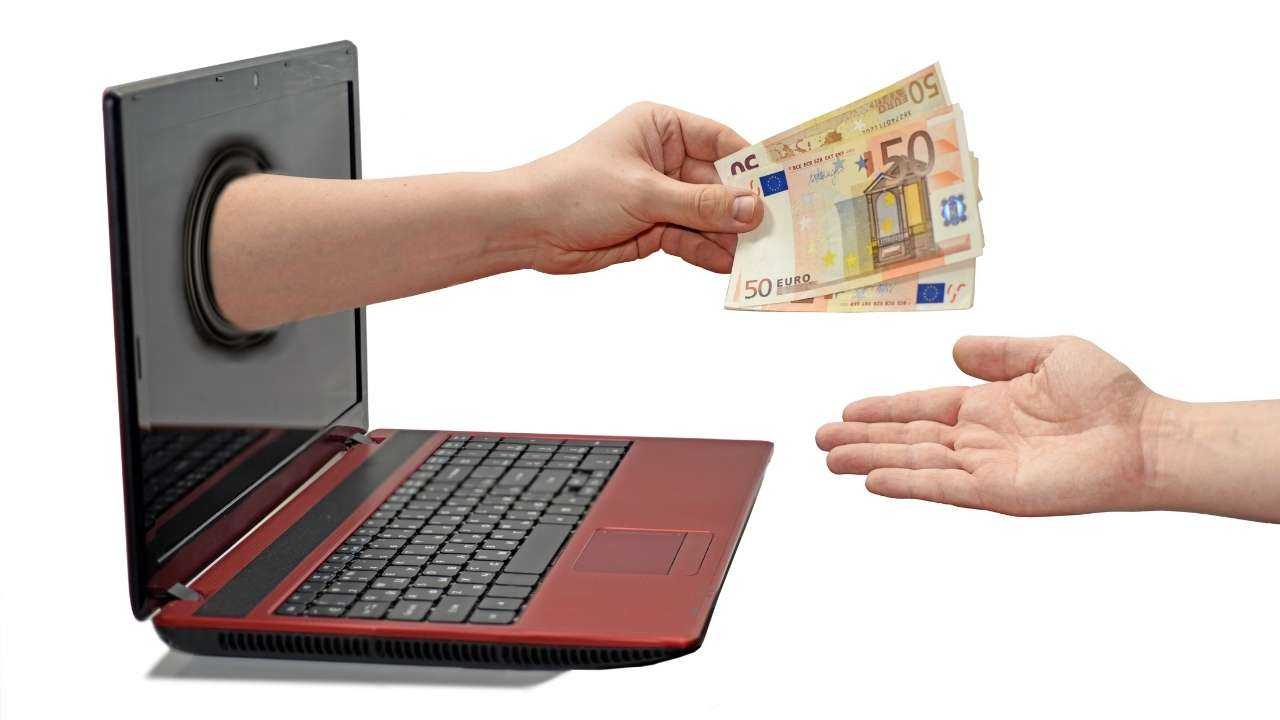 Patēriņa kredīts online ir tikpat ātrs kā attēlā redzamā roka, kas dod naudu no datora ekrāna
