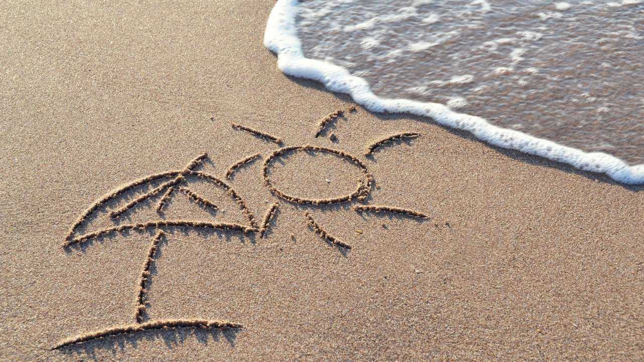 Uz smiltīm pie jūras uzzīmēts saulessargs un saulīte, jo ir sākusies pelnītā atpūta, par kuru saņemta atvaļinājuma nauda